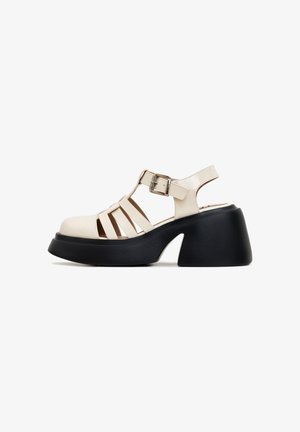 Tykkesorte platform-sandaler med en blank hvid overdel. Har udskårne stropper og en ankelrem for sikker pasform.