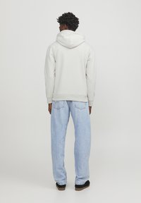 Sudadera con capucha de color gris claro, con un ajuste holgado, combinada con unos vaqueros anchos de color azul claro y zapatillas negras. Textura suave, sin patrones visibles.