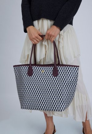 Veľká taška typu tote s námorníckym modrým a bielym geometrickým vzorom, tmavofialovými rúčkami, textúrovanými akcentmi a detailom zlatého kovania v strede.