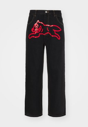 Jeans en denim noir avec un grand graphique rouge d'un chat sautant sur la poche arrière, accentués par des coutures jaunes contrastées le long des coutures.