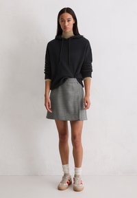 Czarna bluza z kapturem, z regulowanym sznurkiem, w połączeniu z szarym spódnicą w kratę. Kremowe skarpetki z teksturowanym wzorem i beżowe trampki z czerwonymi akcentami.