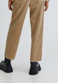 Light brown corduroy pants with vertical stripes, featuring a straight leg cut and back pockets, paired with black platform boots.