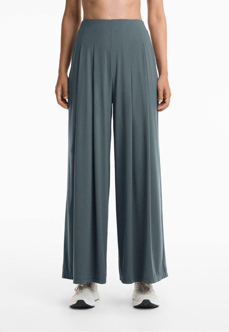 Wijde, geplooide broeken in een gedempte teal kleur. Gemaakt van zacht, vloeiend materiaal. Kenmerkt een hoge taille en een losse silhouet. Gestyled met sneakers.