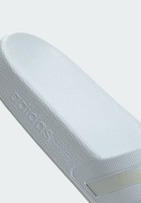 White Adidas slide sandal featuring a textured upper, smooth footbed, and a metallic silver accent stripe along the side.