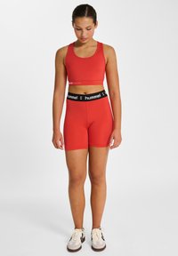 Czerwony sportowy crop top i dopasowane szorty wykonane z elastycznego materiału, z czarnym ściągaczem z logo "hummel". Płaskie szwy, dopasowany krój.