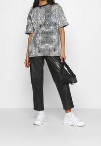 Czarno-biała koszulka w wężowy wzór, z krótkimi rękawami, połączona z czarnymi spodniami z sztucznej skóry i białymi sneakersami. Trzyma czarną torebkę.