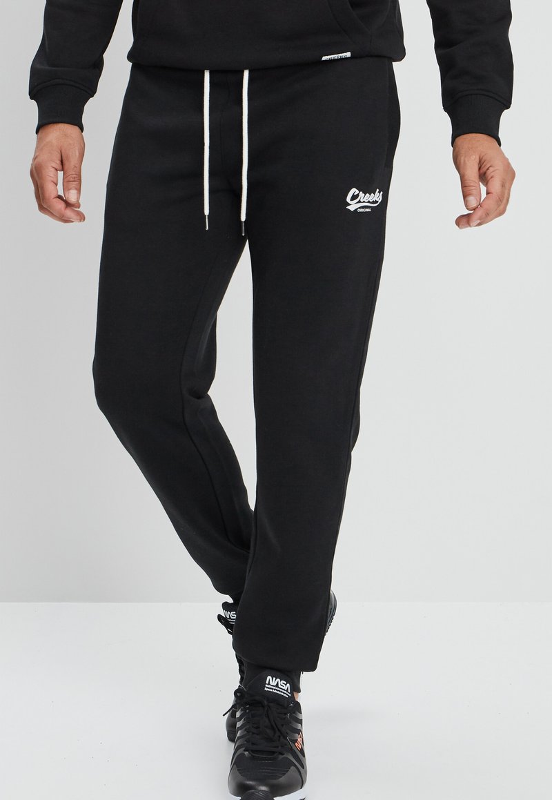 Zwarte sweatpants met een relaxte pasvorm, voorzien van witte koordjes, zijzakken en een klein logo-detail op de dij.