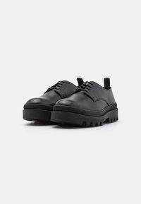 Chaussures en cuir noir à bout arrondi, design à lacets et semelle en caoutchouc épaisse avec un motif texturé en stries.