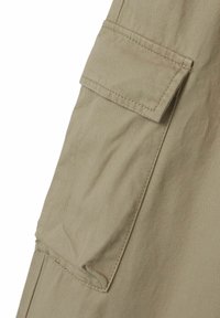 Beige cargo tasku nappiläppätiedoilla vaatteiden vasemmalla puolella. Materiaali näyttää kevyeltä ja teksturoidulta, ja näkyvät tikkausjäljet ovat selvästi erottuvia.