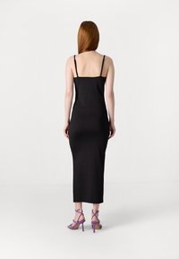 Černé, přiléhavé midi šaty s tenkými nastavitelnými ramínky. Hladká textura, jednoduchý design. V kombinaci s fialovými sandály na vysokém podpatku se řemínky.