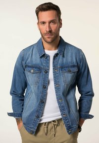 Denimjacka i medelblått med framfickor, knäppning med knappar och kontrasterande sömmar. Stylad över en vit skjorta, med en avslappnad passform.