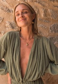 Olive green, textured fabric dress with deep V-neck and gathered waist. Gold pendant necklace and drop earrings complement the look.