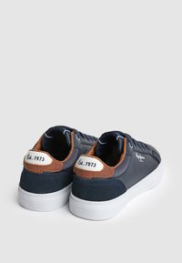 Tumesinine tennisekad tan-suede aktsentide, valge kummitald ja tikkimise detailid. Omab logo ja "Est. 1973" sildi kontsapooles.