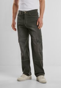 Pantalones cargo en denim gris oscuro con costuras en contraste, ajuste holgado y bolsillos laterales. Combinados con zapatillas de color claro.