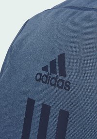 Adidas backpack in dark blue fabric, featuring a textured surface, embossed logo, and three vertical black stripes design.