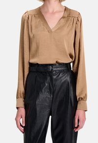Blouse en satin beige avec un col en V, des épaules plissées et des manches longues associée à un pantalon en cuir noir taille haute.