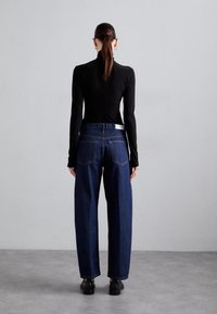 Tmavě modré rifle s vysokým pasem a širokou nohavicí, doplněn é přiléhavým černým topem s dlouhým rukávem. Bílý opasek jako akcent, minimalizované švy.