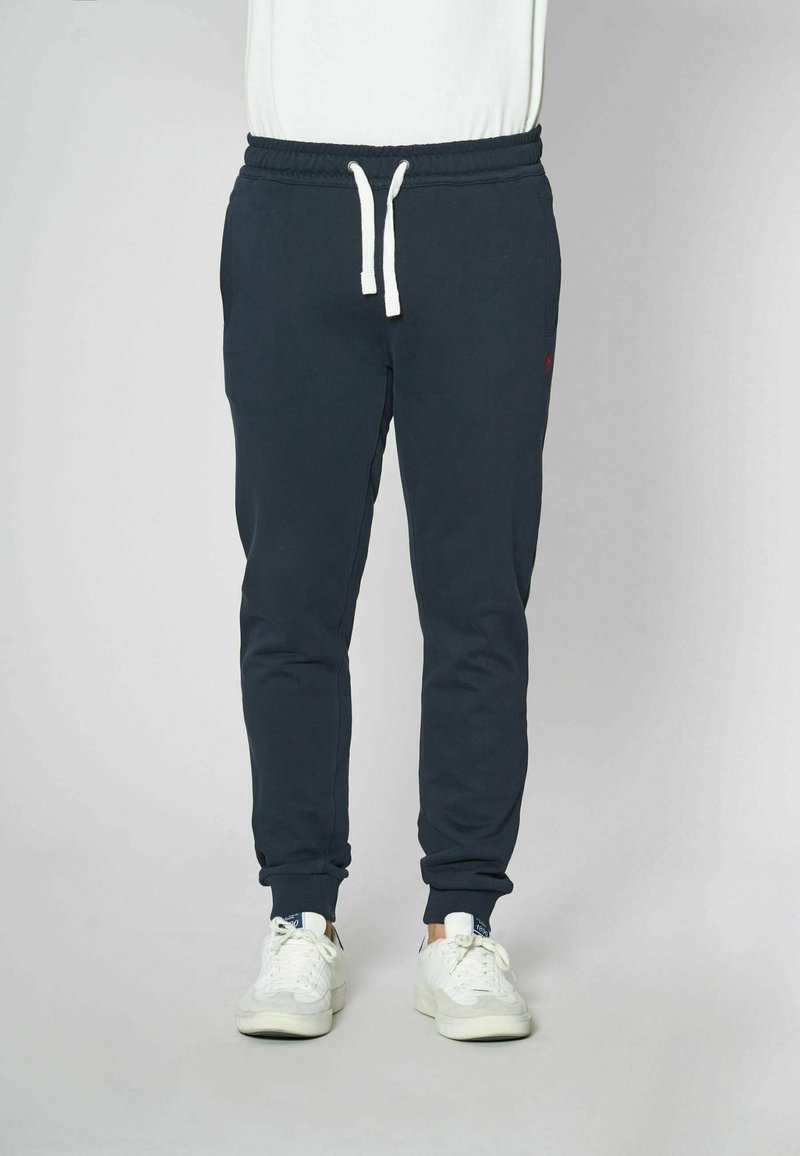 Pantaloni jogger blu navy con vita regolabile, dotati di tasche laterali e polsini a coste, realizzati in un tessuto morbido. Dettaglio del logo piccolo.