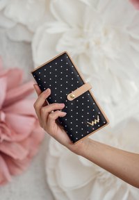 Black polka dot wallet with a light pink leather accent; features a snap closure and a gold logo detail on the front.