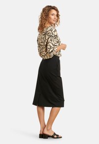 Zwarte rok met een zijsplit, gecombineerd met een beige blouse met een zwart abstract bloemenpatroon. Soepele stof, losse pasvorm, korte mouwen.