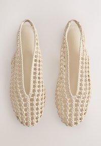 Paire de chaussures plates à bride arrière tissée beige avec un design en treillis ouvert et un bout arrondi sur un fond uni.