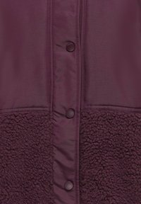 Veste violet foncé avec boutons-pression et combinaison de panneaux en polaire lisse et texturée.