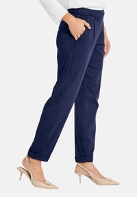 Marineblauwe tapered broek met een elastische tailleband, zijzakken en opgerolde mouwen, gecombineerd met beige hoge hakken. Zachte stoftextuur.