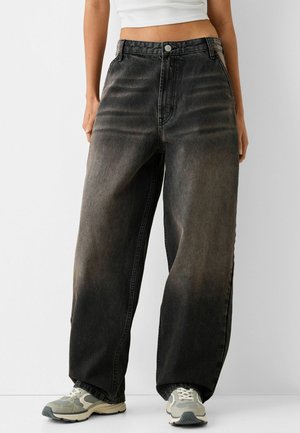 Wide-leg faded black jeans worn with white sneakers and a cropped white top, showing midriff and hands at sides.