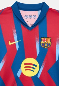 Az FC Barcelona mez vörös és kék cikk-cakk mintákkal. Légáteresztő anyagból készült, V-nyakú, sárga Nike logóval és Spotify emblémával.