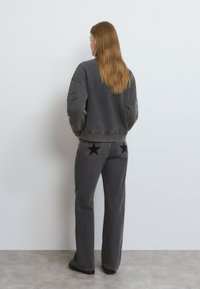 Sudadera gris de gran tamaño con parches de estrellas y jeans grises de cintura alta que presentan apliques de estrellas oscuras en los bolsillos traseros.