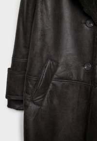 Cappotto in shearling nero con texture liscia, ampio colletto e chiusura a bottone, dotato di tasca laterale integrata per funzionalità.