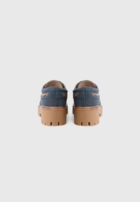 Blaue Canvas-Schuhe mit gepolstertem Obermaterial, zwei seitlichen Akzenten und klobigen braunen Gummisohlen mit einem strukturierten Muster für besseren Halt.