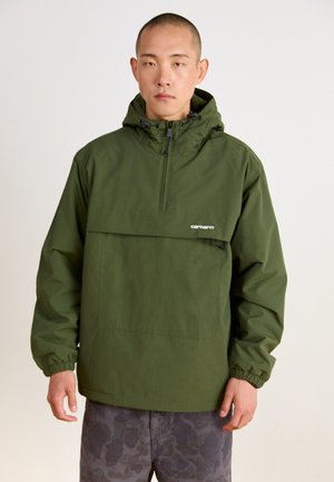 Chaqueta de pullover verde oliva con capucha, medio cierre frontal, puños elásticos y un bolsillo frontal; el tejido parece suave y ligero.
