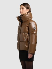 Brun vadderad jacka med hög krage, glansigt ytskikt, quiltad struktur och detaljer med dragkedjefickor. Buren över en svart ribbad kjol.