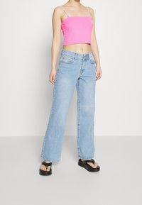 Jasnoróżowy prążkowany top na ramiączkach, w zestawie z jasnoniebieskimi dżinsami o szerokich nogawkach i czarnymi platformowymi klapkami.
