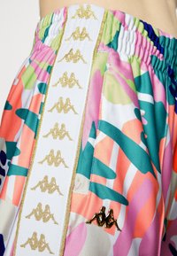 Pantalones cortos coloridos y con patrones que presentan una mezcla de rosa, verde y azul, con un panel lateral blanco que muestra logotipos y ribetes dorados de Kappa.