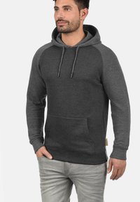 Hoodie gris foncé avec une poche kangourou, une capuche à cordon de serrage et des manches raglan gris clair contrastantes. Texture douce et poignets côtelés.