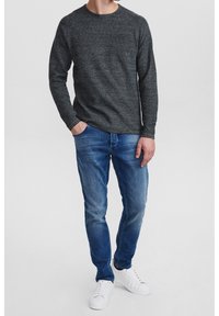 Mörkgrå texturerad stickad tröja med rund hals, ihop med urtvättade blå jeans och vita sneakers, händerna i fickorna.