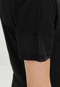 Svart skjorta med korta ärmar som har en strukturerad meshdetalj i nederkanten. Mjuk tyg med en något genomskinlig utseende.