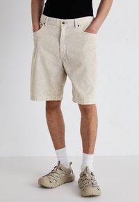Lys beige kordfløjl shorts med lodrette striber, der har forlommer, knaplukning og lige pasform. Bæres med beige sneakers.