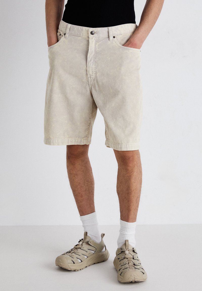 Lys beige kordfløjl shorts med lodrette striber, der har forlommer, knaplukning og lige pasform. Bæres med beige sneakers.