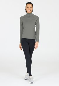 Langærmet, kvart-zip top i lysegrå, parret med sorte leggings og grå athletic sko. Glat stof med en tætsiddende pasform.