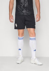 Sorte sportskort med et tekstureret blomstermotiv, parret med hvide sokker med blå striber og hvide sportssko med en blank finish.