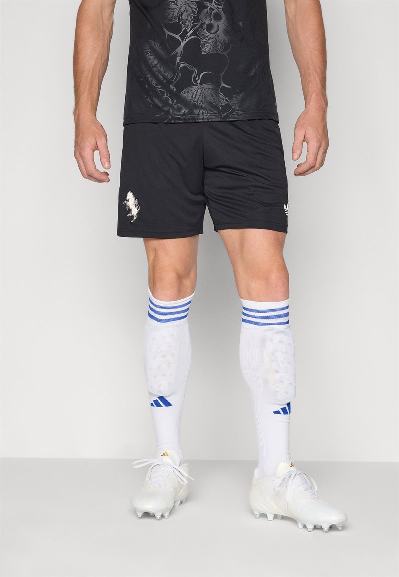 Sorte sportskort med et tekstureret blomstermotiv, parret med hvide sokker med blå striber og hvide sportssko med en blank finish.
