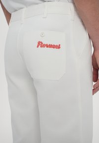 Bijele traperice s natrag džepom i crvenim izvezenim tekstom "Fiorucci". Ravnog kroja s vidljivim šavovima i detaljima na dugmetu.
