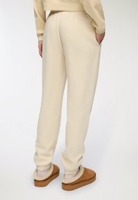 Beżowe dresy z elastycznym pasem, bocznymi kieszeniami i zwężanymi mankietami, w połączeniu z jasnobrązowymi klapkami z miękkim, futrzanym wykończeniem.