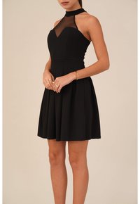 Černé šaty ve stylu fit-and-flare s halenkou z síťoviny a rozšířenou sukní. Hladká látka, přiléhavá korzetová část a jemné sklady v pase.