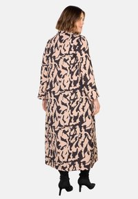 Lungo vestito beige con un motivo astratto nero, caratterizzato da maniche lunghe e una linea dritta, abbinato a stivaletti neri con tacco.