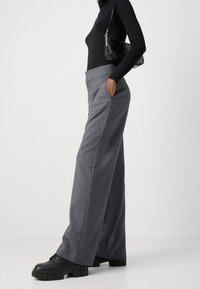 Pantalons gris à jambes larges avec un tissu texturé et des poches latérales, associés à des chaussures à plateforme noires et à un sac à main noir.