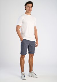 T-shirt bianca a maniche corte, pantaloni corti a quadri blu scuro con risvolti e scarpe da ginnastica grigie con dettagli colorati. Outfit semplice e casual.